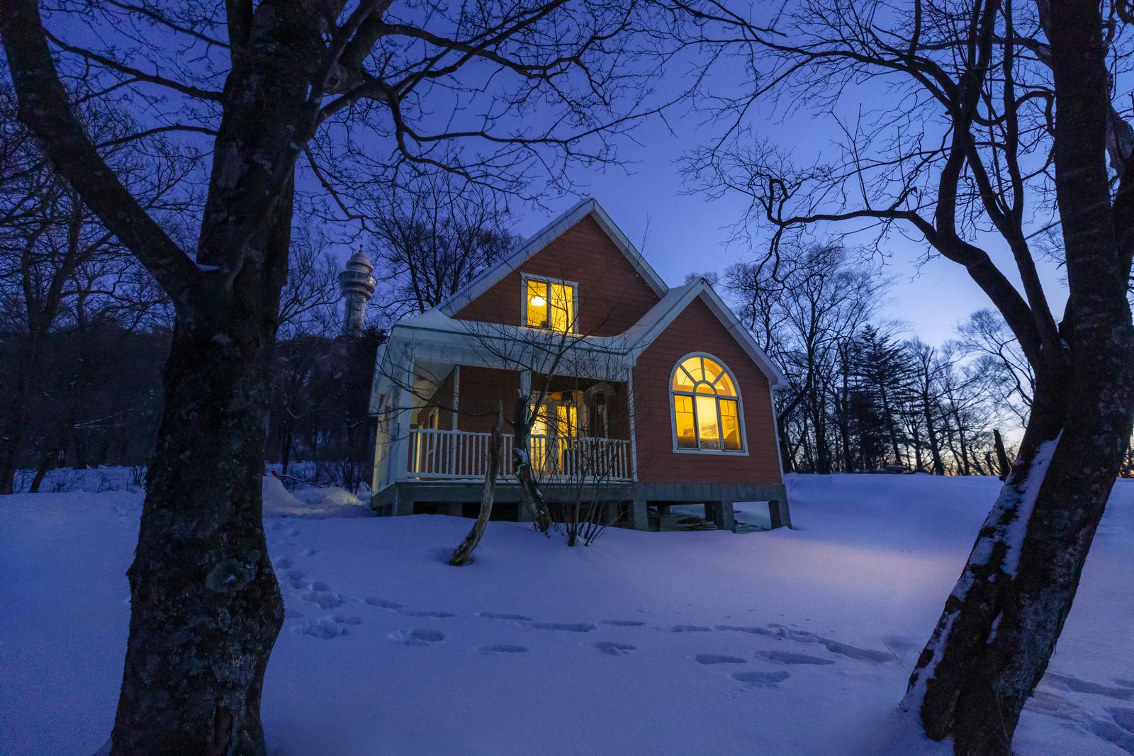 A cabin glowing warmly among snowy trees at twilight